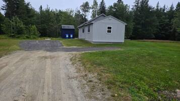 A gravel driveway leading to a small, single-story building with a gray exterior and a window.