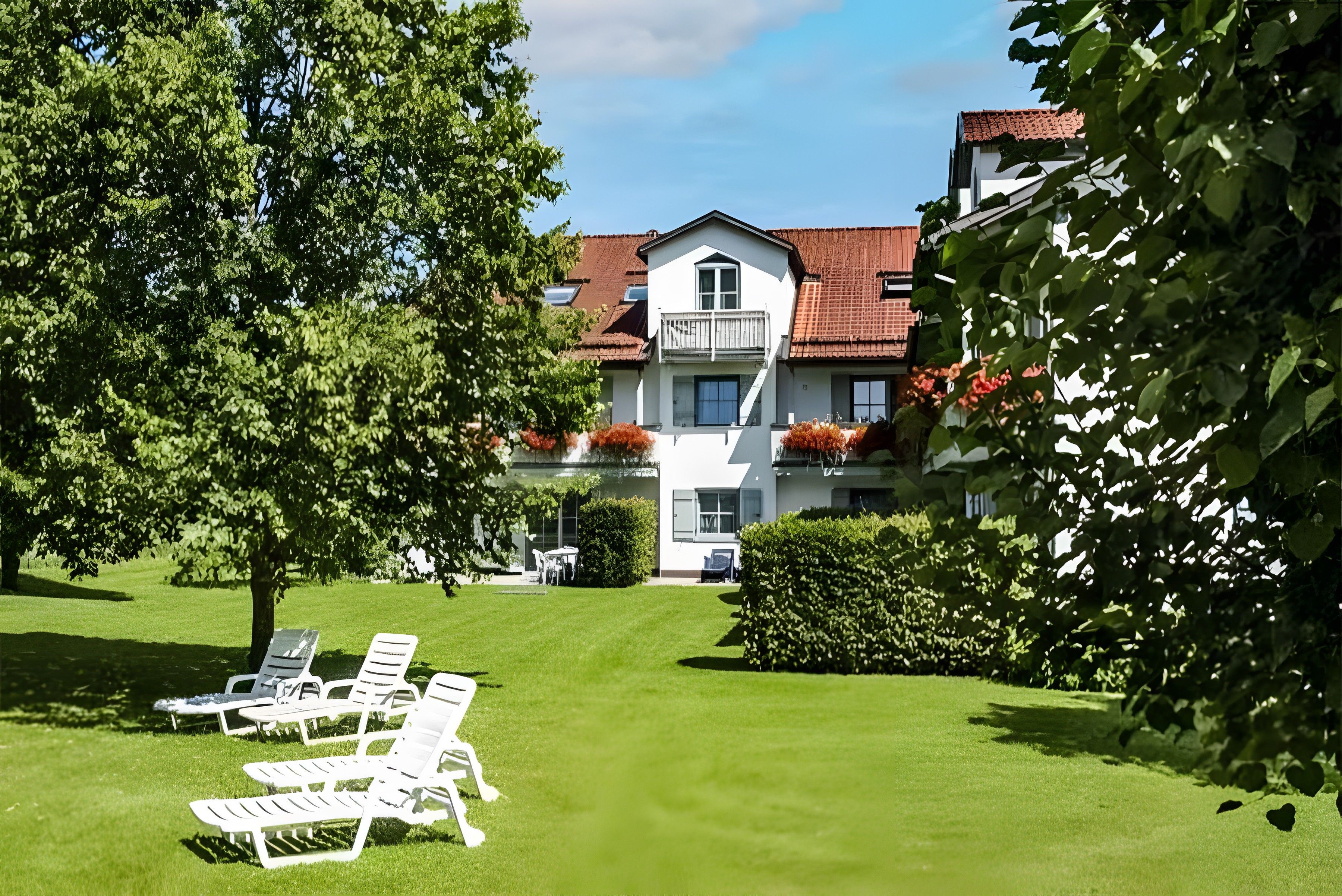 Un hôtel doté d’une pelouse bien entretenue, d’un espace extérieur aménagé pour s’asseoir et d’un bâtiment surmonté d’un toit recouvert de tuiles rouges.