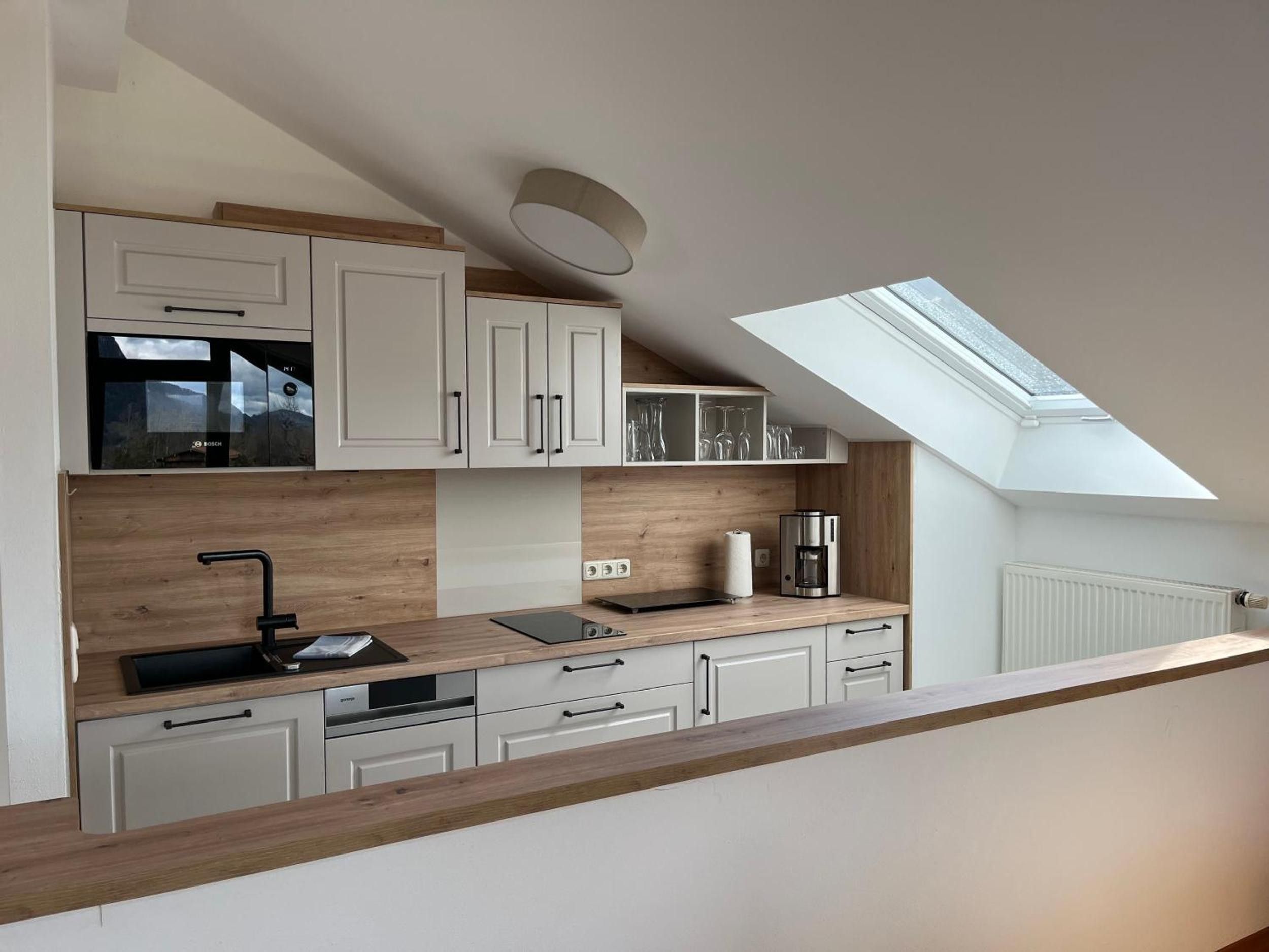Una cocina moderna con armarios blancos, encimera de madera, una cafetera y un tragaluz.