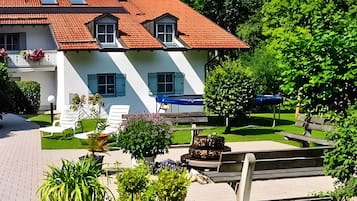 Un bâtiment à deux étages, doté d’un toit recouvert de tuiles rouges, d’un jardin avec une fontaine et d’un espace extérieur aménagé pour s’asseoir.