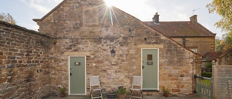 A stone building with two green doors, a bench, and potted plants.