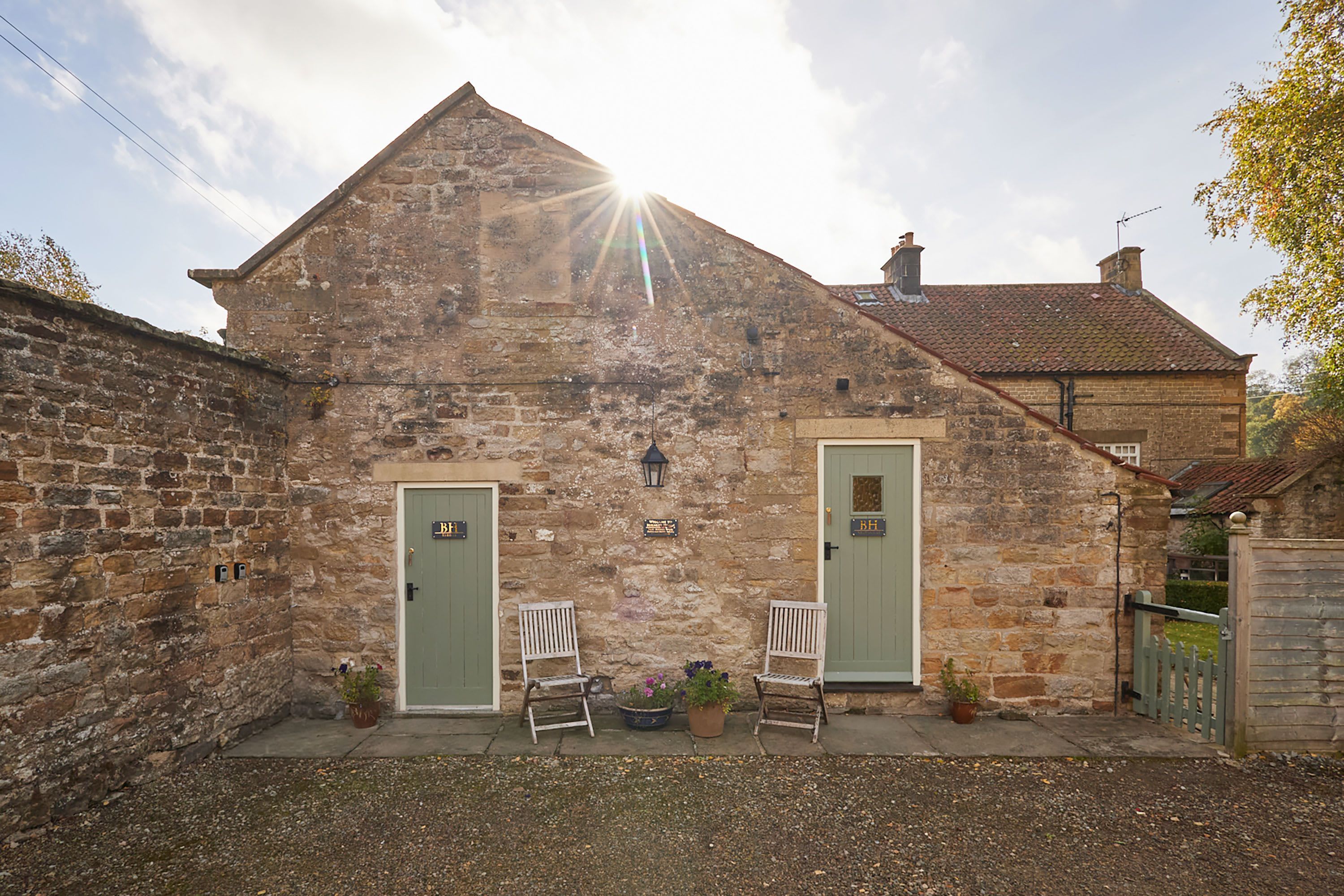 A stone building with two green doors, a bench, and potted plants.