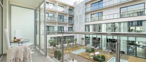 En modern hotellbalkong med ett glasräcke, vita möbler och utsikt över innergården nedanför.