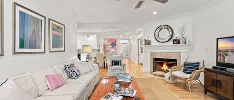 A spacious living room with a fireplace, a ceiling fan, and a television.