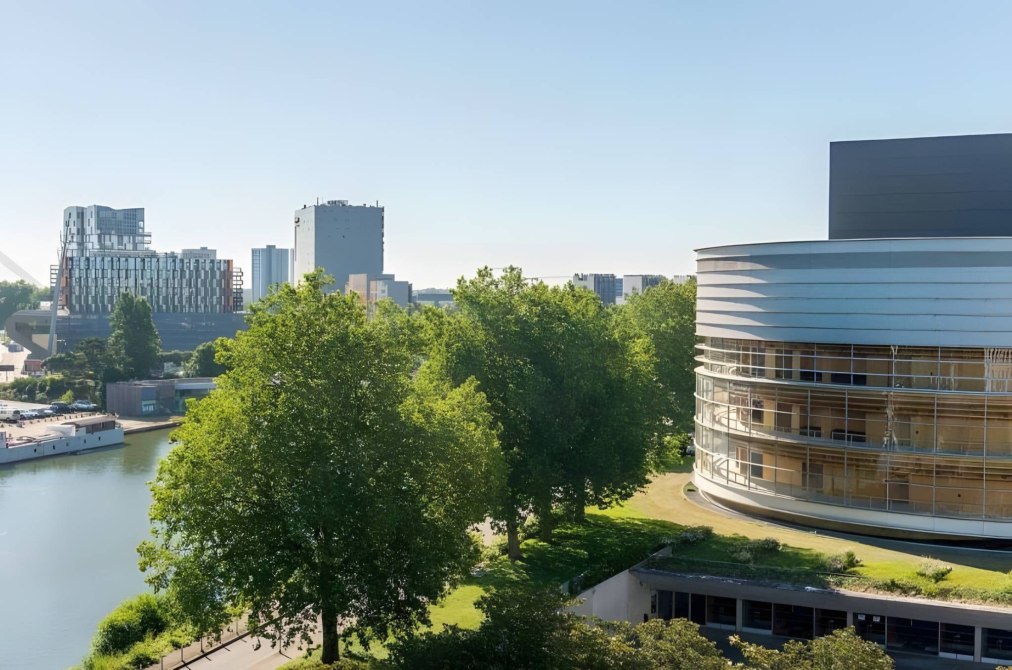 Un edificio moderno con facciata curva, affiancato da un fiume e alberi verdi e rigogliosi sullo sfondo.