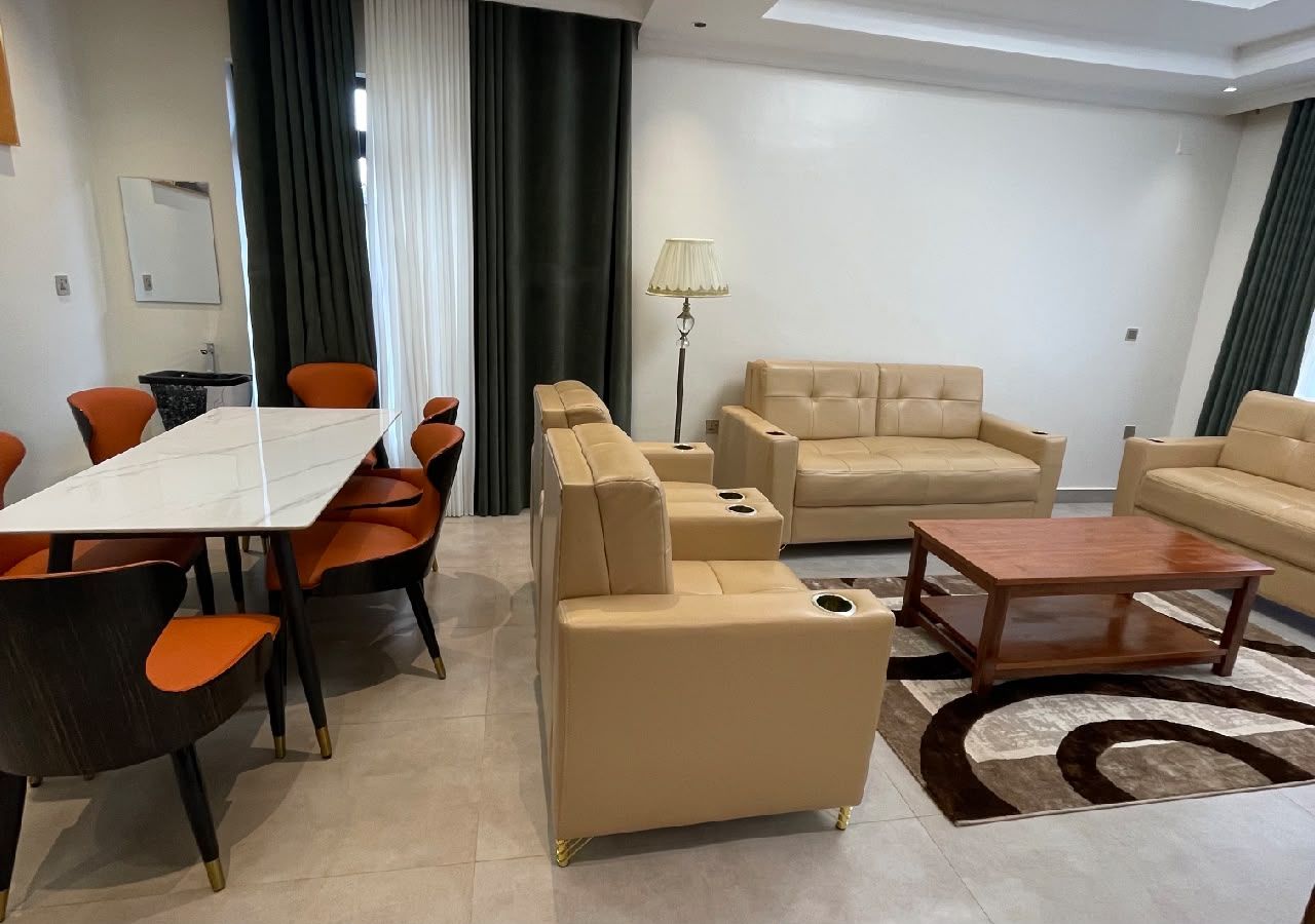 Un salon moderne comprenant un coin repas, des canapés de couleur beige, une table basse et un tapis à motifs.