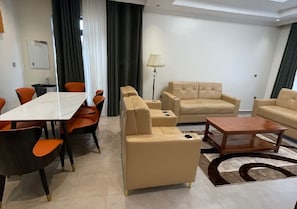 A modern living room with a dining area, beige sofas, a coffee table, and a patterned rug. - DAKA LUXURY APARTMENTS (Kigali)