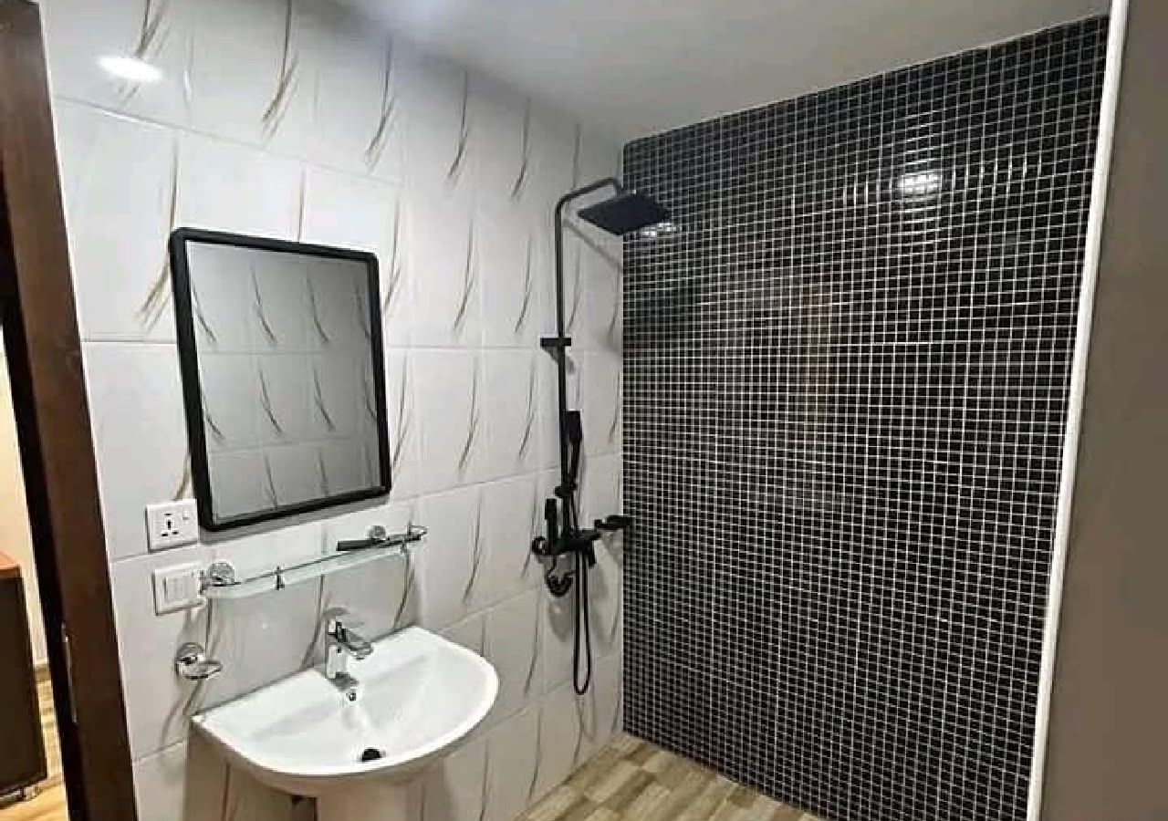 Une salle de bain avec un lavabo blanc, un miroir et une douche aux carreaux noirs.