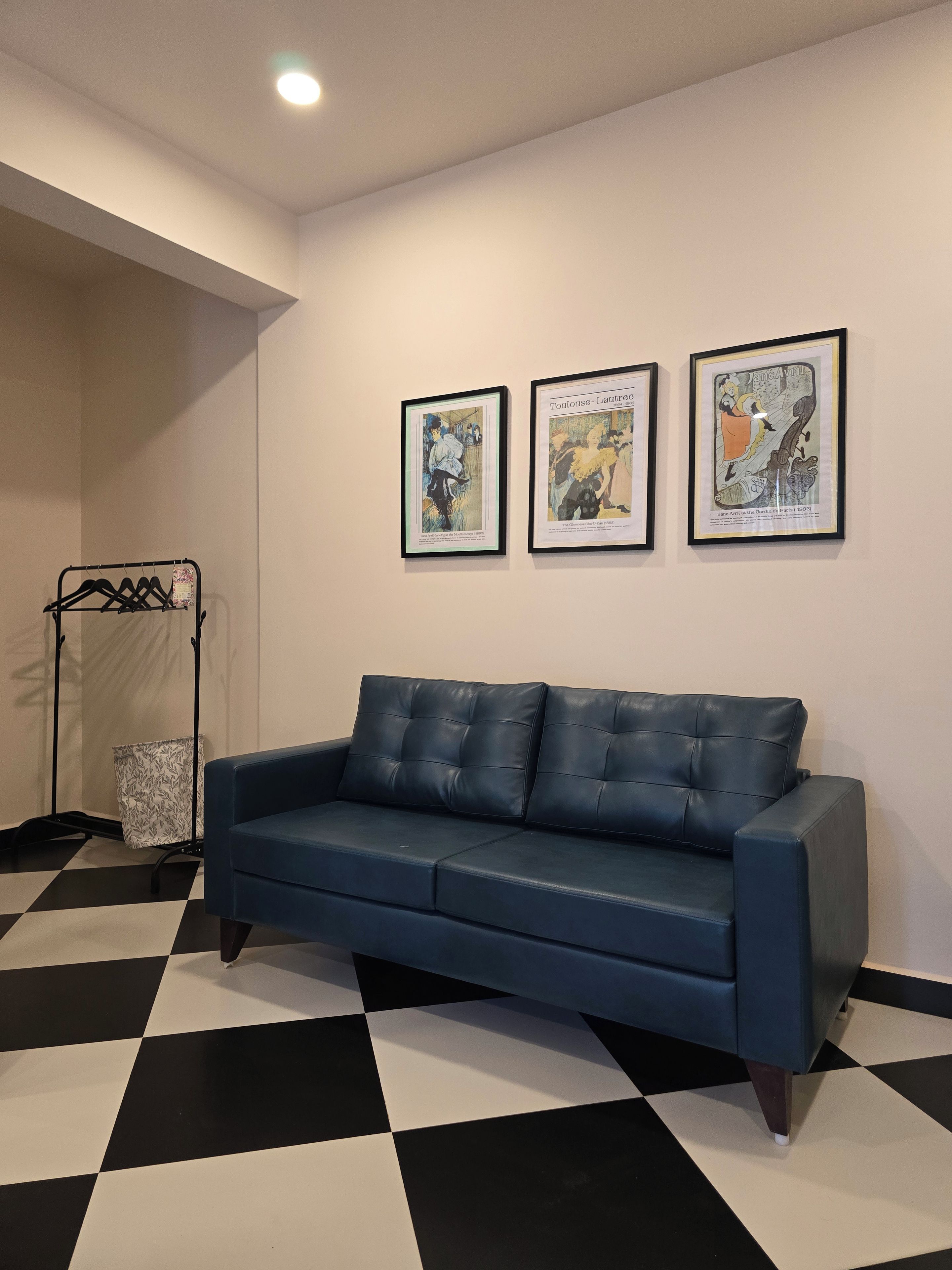 Une pièce avec un canapé bleu, un sol à carreaux et trois œuvres d’art encadrées accrochées au mur.