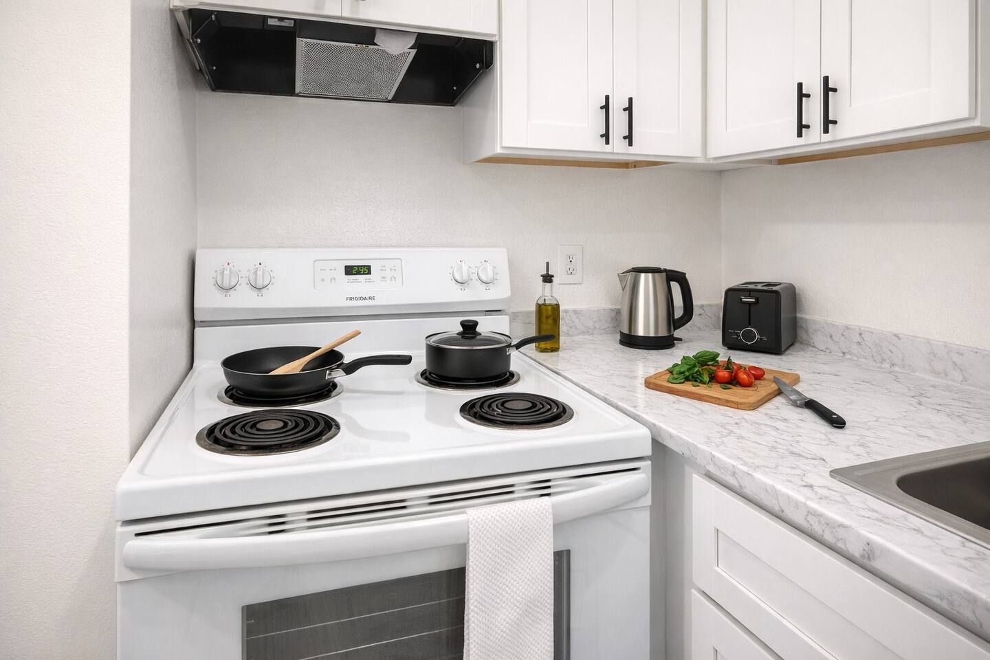 A kitchen with a white stove, a kettle, a toaster, and a cutting board with vegetables.