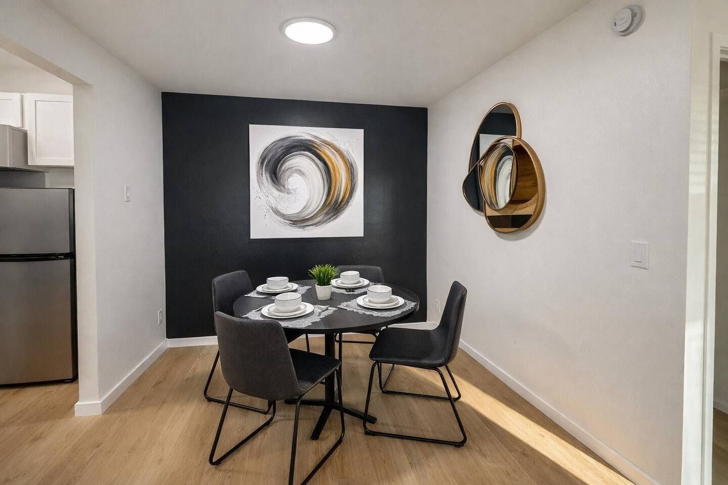 Una zona de menjador moderna amb un quadre abstracte en blanc i negre, una taula rodona amb cadirees i un forn integrat.