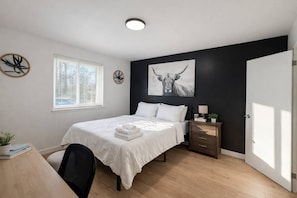 Un dormitorio con cama, mesita de noche, lámpara y una obra de arte.