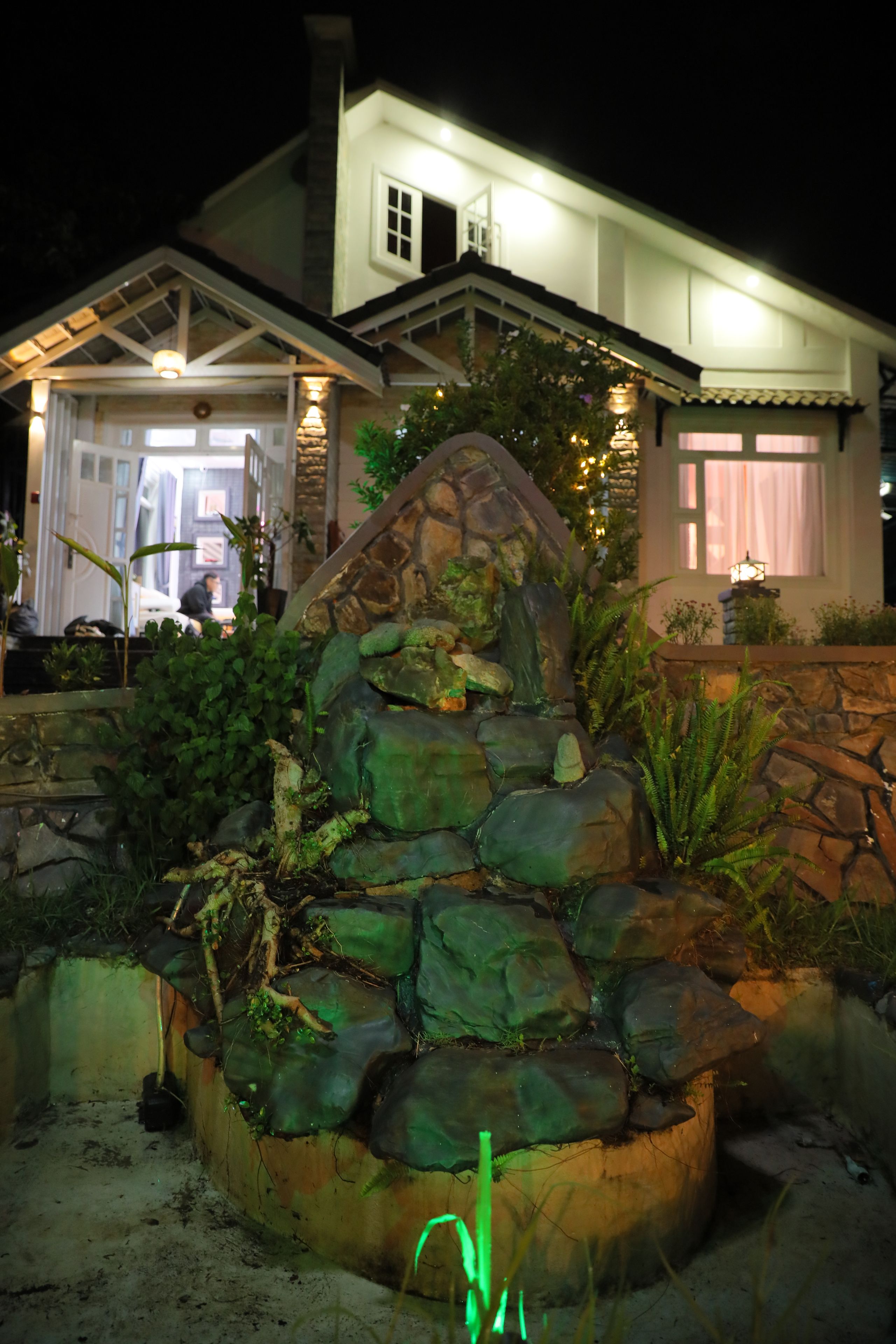 A stone waterfall feature in a landscaped garden area with a house in the background.