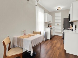 A compact kitchen with white cabinets, a dining table with a placemat, and a small island with a sink. - Charming + Romantic Downtown Hideaway in the Heart of Historic St. Augustine! (St. Augustine)