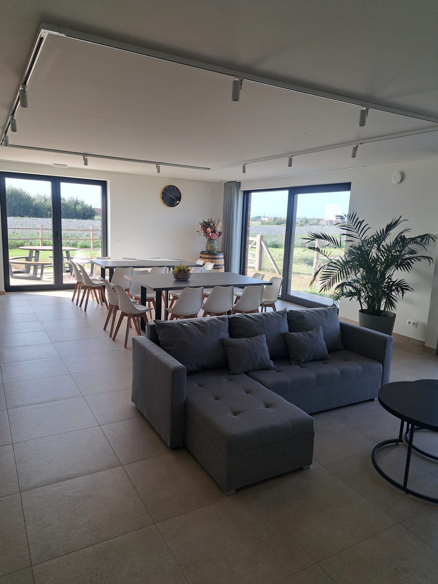 Un salón amplio con un sofá modular, una mesa de comedor con sillas y ventanas grandes con vistas al exterior.