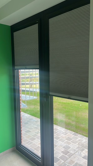 A room with a large sliding glass door leading to an outdoor area with a paved patio and a grassy lawn.