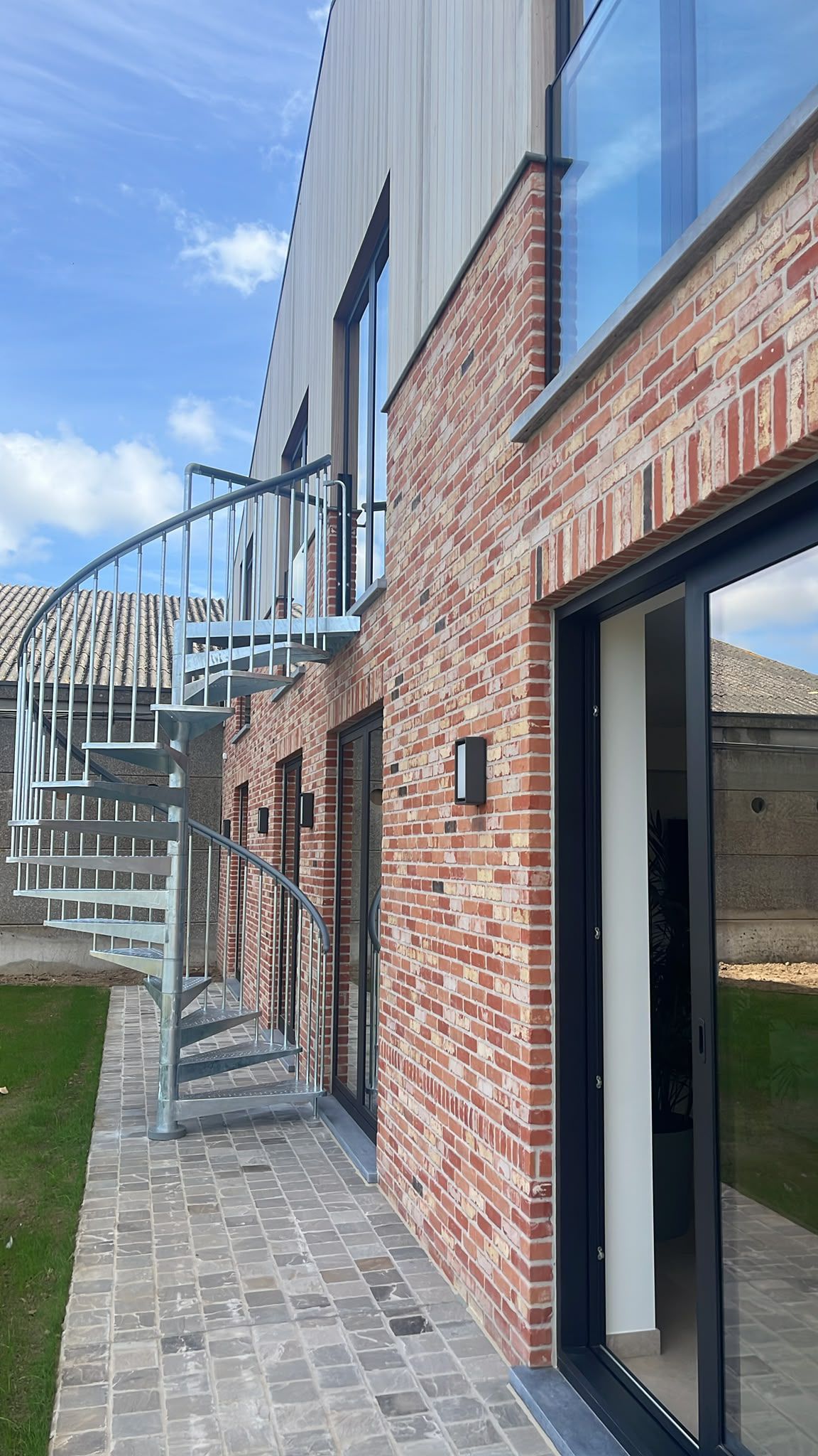 A modern building with a brick facade, a spiral staircase, and large glass doors.