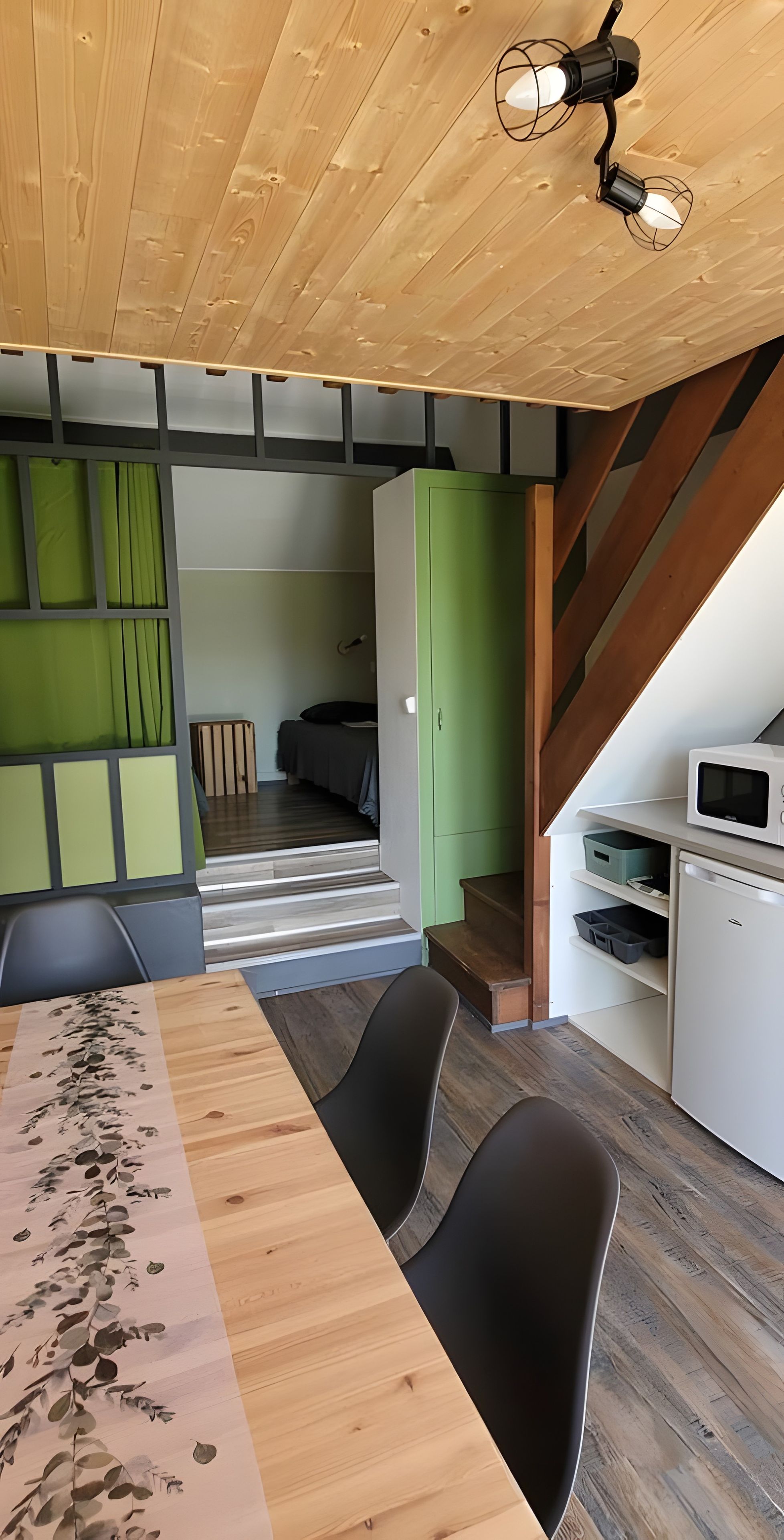 Un intérieur moderne avec un plafond en bois, un coin repas comprenant une table et des chaises, un coin cuisine et un mur d’accent de couleur verte.