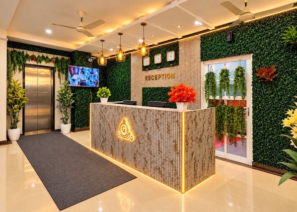 A reception area with a wooden reception desk, a flat-screen TV, and a green wall with plants.