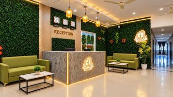 Et receptionområde med en træreception, grønne sofaer, et sofabord og en væg med ure og planter.