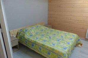 A small, single-bed room with a wooden headboard, a bedside table, and a plain wall.