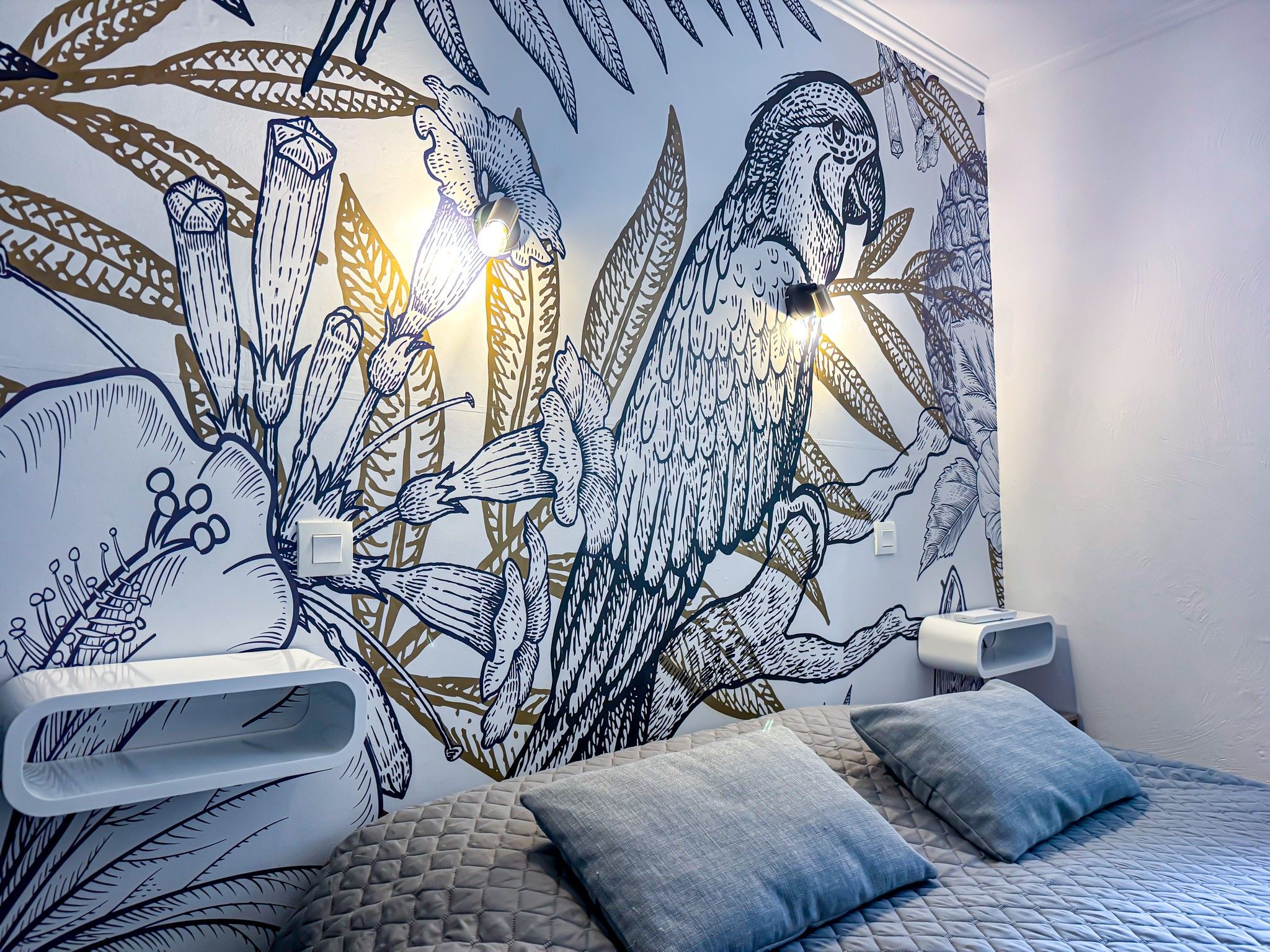 Ein Schlafzimmer mit Wandgemälde, einem Bett mit gesteppter Bettdecke und Nachttischen mit Lampen.