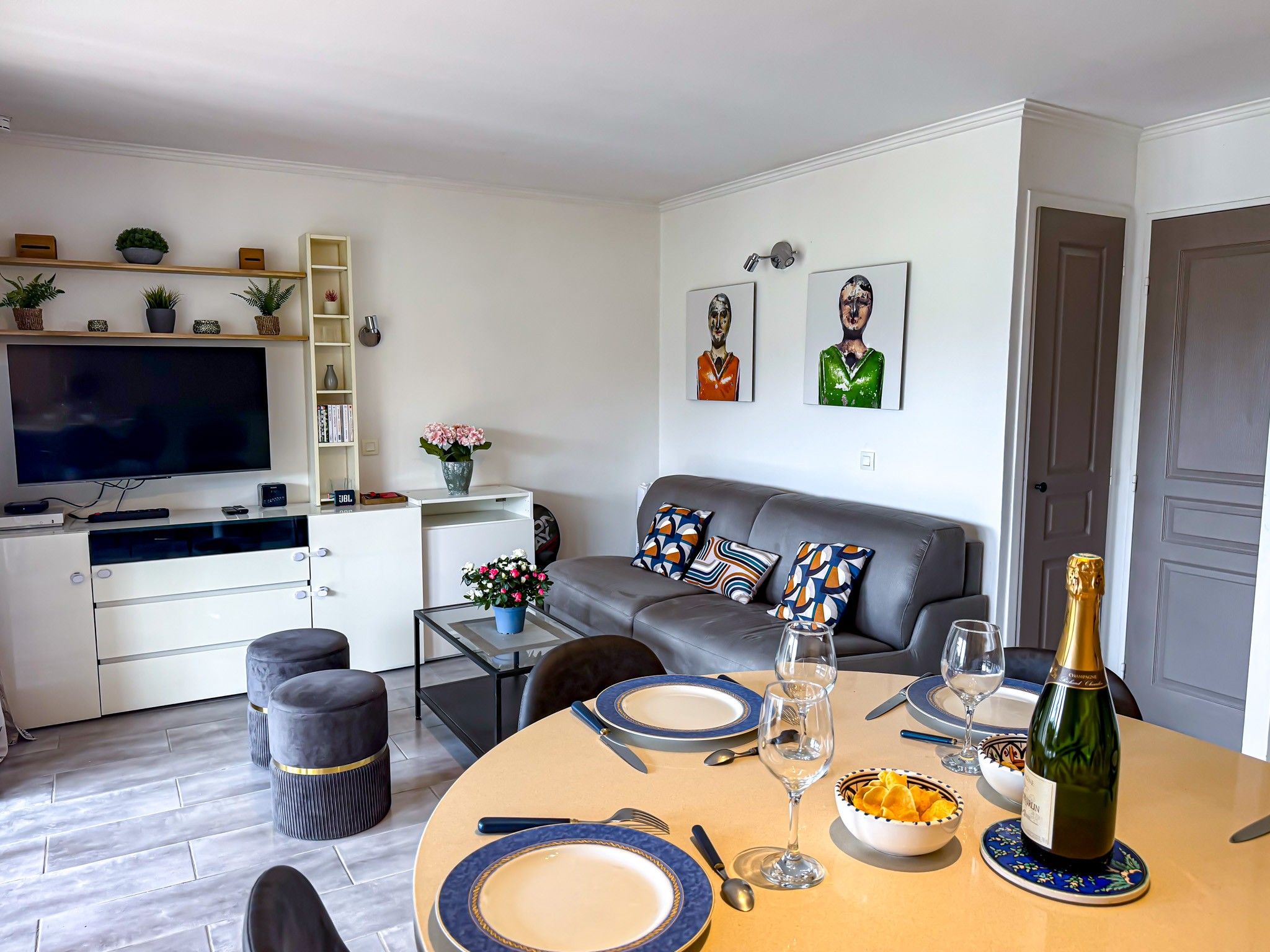A modern living room with a sofa, a dining table set for two, and a television.