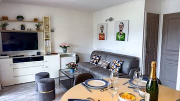 A modern living room with a sofa, a dining table set for two, and a television.