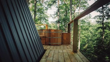 Une terrasse en bois avec un jacuzzi et une structure métallique, le tout entouré d’arbres.