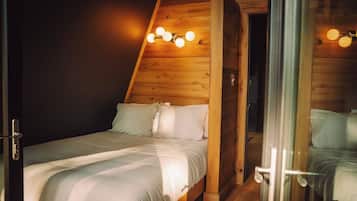 Un dormitorio con techo inclinado, una cama con ropa de cama blanca y una lámpara fijada a la pared.