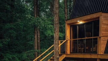 Una cabaña de madera con una escalera que conduce a una terraza, rodeada de árboles.