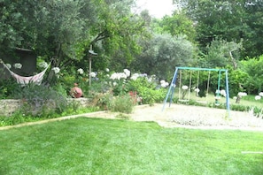 Un jardí amb un tobogan, un hamaca i diverses plantes i flors.