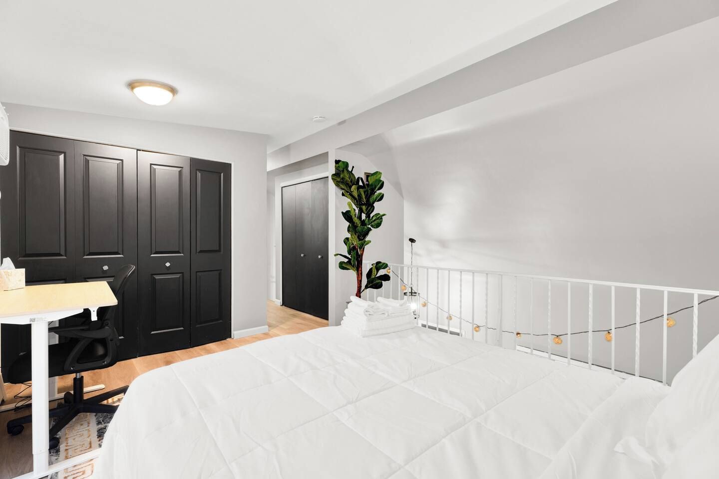 A bedroom with a bed, a desk, and a chair. There are two doors and a plant.