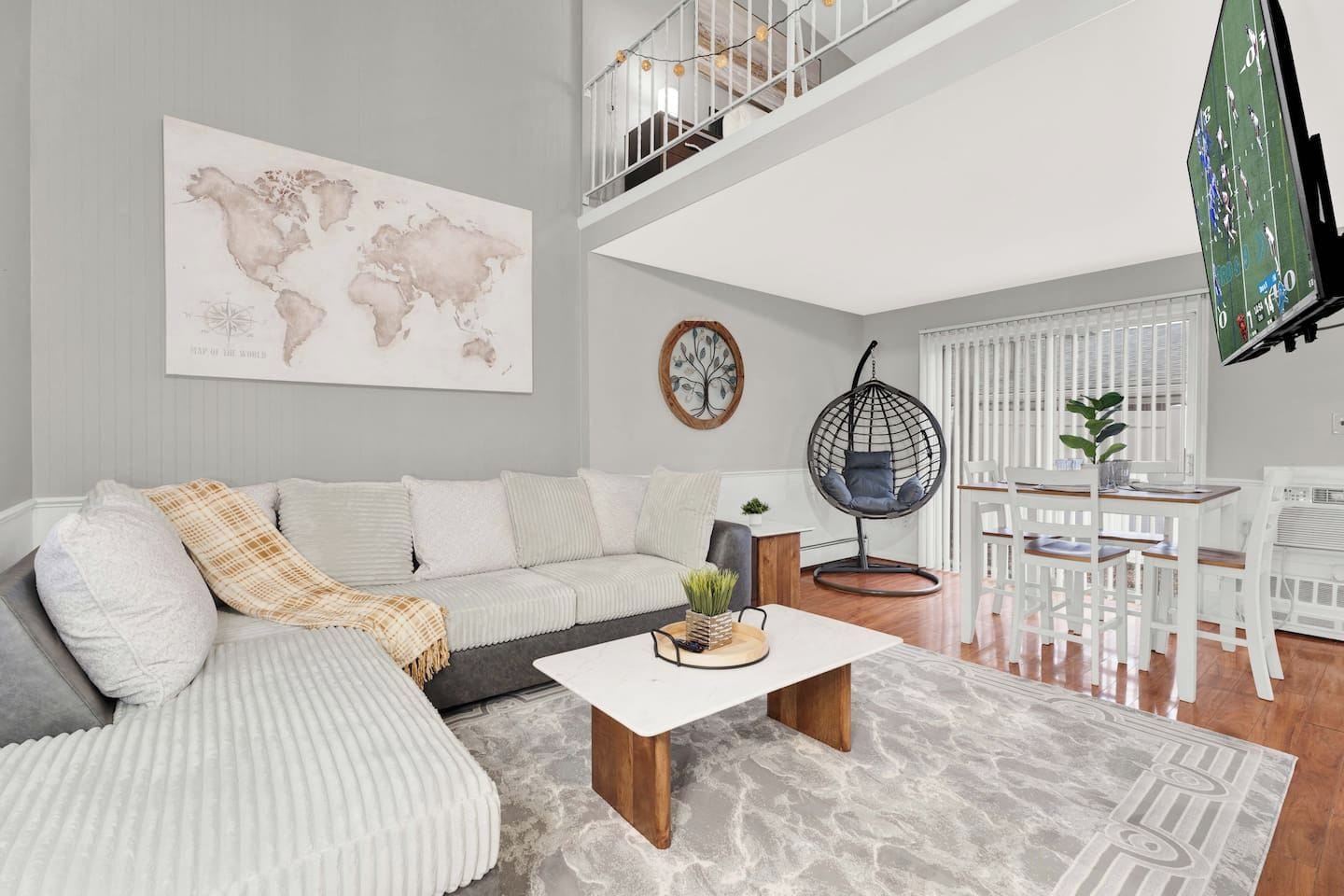 Una sala moderna con sofá, mesa de centro y sillón colgante. Un mapa del mundo adorna la pared, y hay un televisor también.