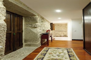 Un passadís amb paret de pedra, porta de fusta i un moquet a peu d'una habitació.