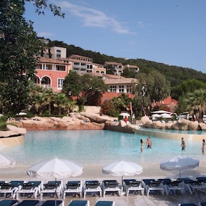 Un espace piscine doté de chaises longues et de parasols, entouré de bâtiments et de verdure.
