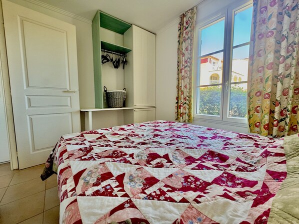 Un dormitorio con cama, armario, ventana con cortinas y vistas al exterior.
