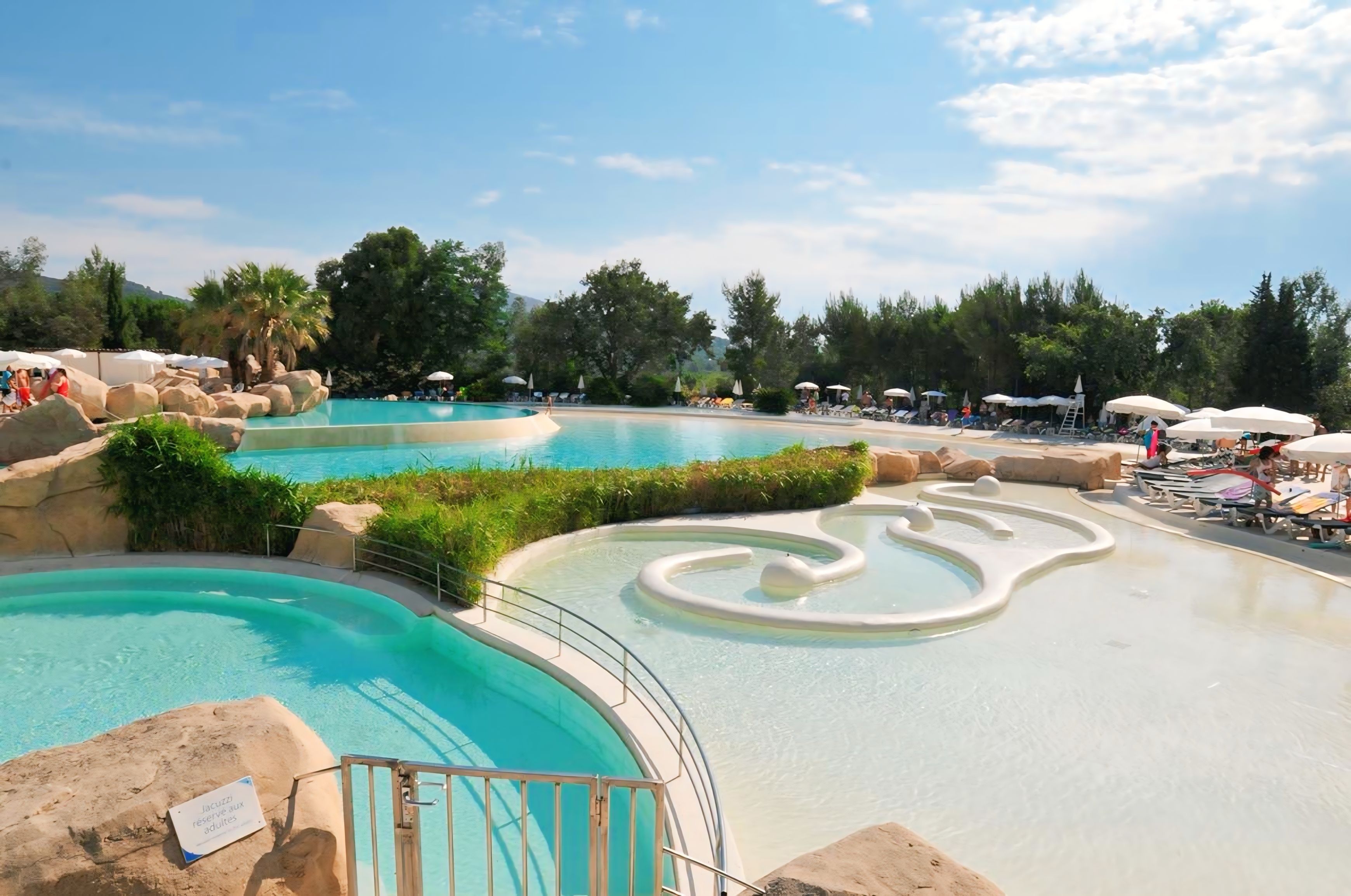 Une grande piscine extérieure dotée de plusieurs couloirs de nage et entourée d’une zone aménagée avec des chaises longues et des parasols.