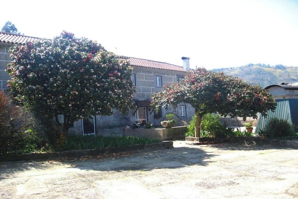 A stone building with a tiled roof, surrounded by a gravel driveway and two flowering trees. - New Listing (Braga)