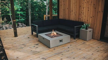 Une terrasse en bois avec un foyer, un canapé noir et un petit pot de fleurs.