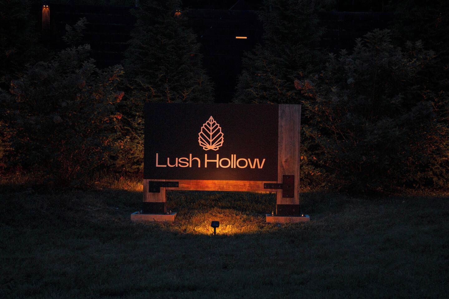 Une enseigne avec le texte « Lush Hollow » et un logo représentant une feuille, le tout sur un fond sombre aux bords illuminés.