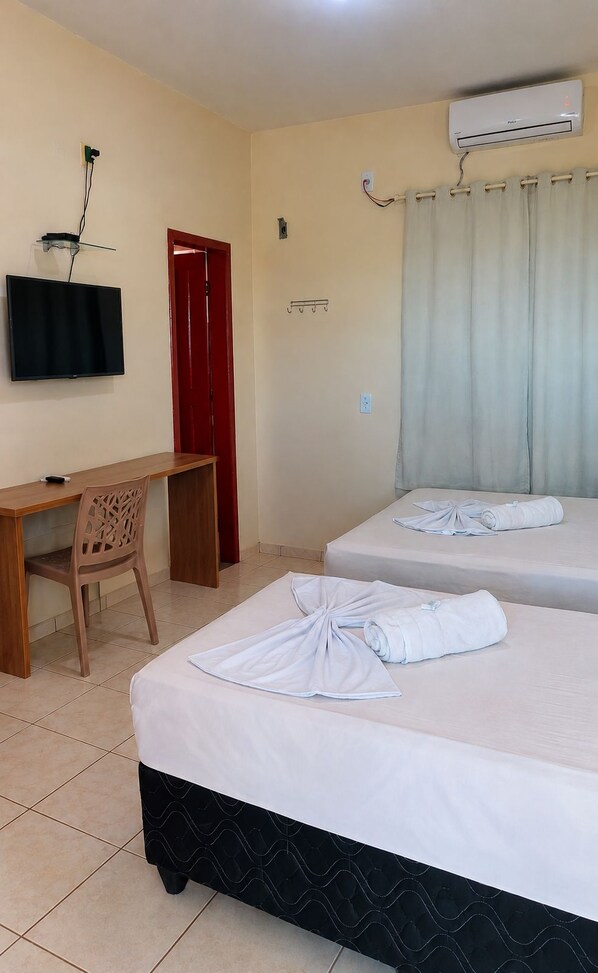 Una habitación de hotel con dos camas, un escritorio, una silla, un televisor y un aire acondicionado.