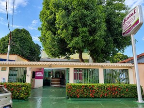 Entrada de un hotel con un árbol grande, una recepción y un letrero.