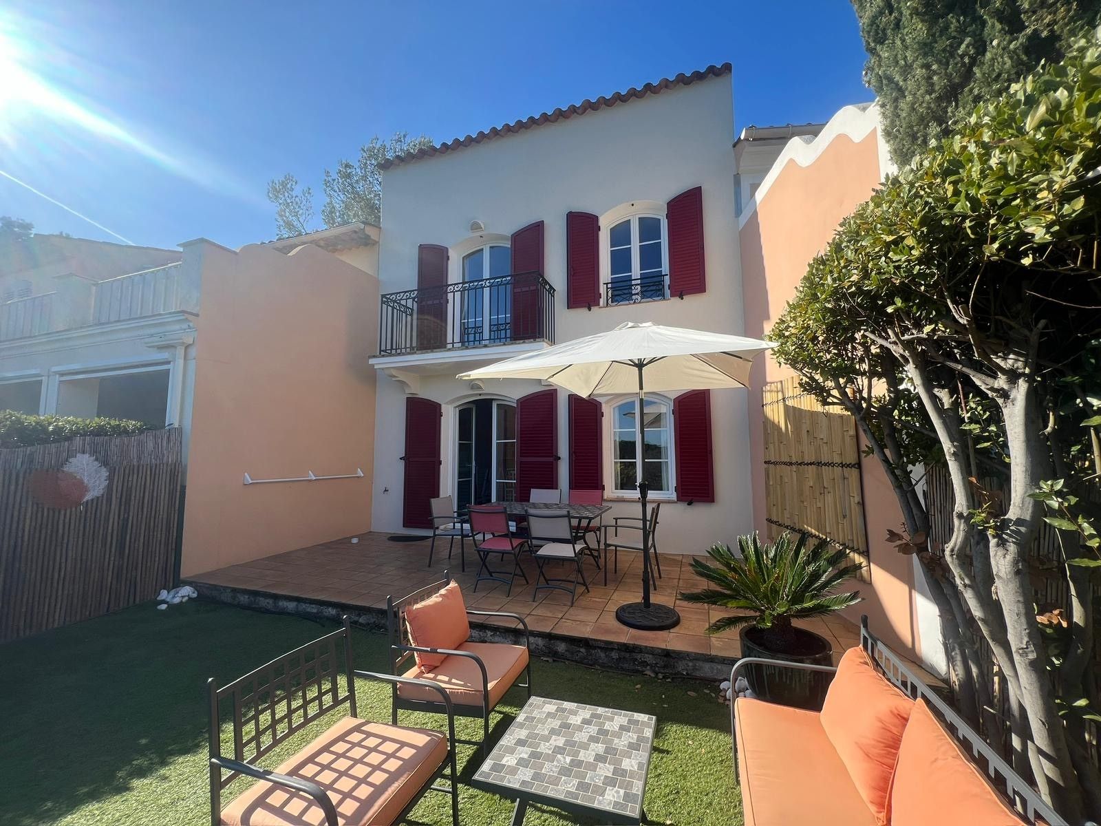 A two-story house with a balcony, a patio with outdoor furniture, and a small garden area.