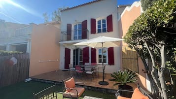 A two-story house with a balcony, a patio with outdoor furniture, and a small garden area.