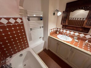 Une salle de bain avec une baignoire blanche, un lavabo avec un miroir au-dessus et un luminaire fixé au mur.