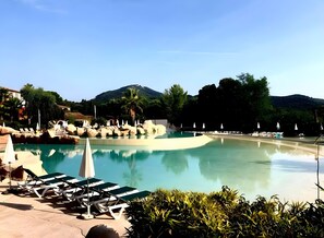 Un espace piscine agrémenté de chaises longues et de parasols, entouré de rochers et de verdure.
