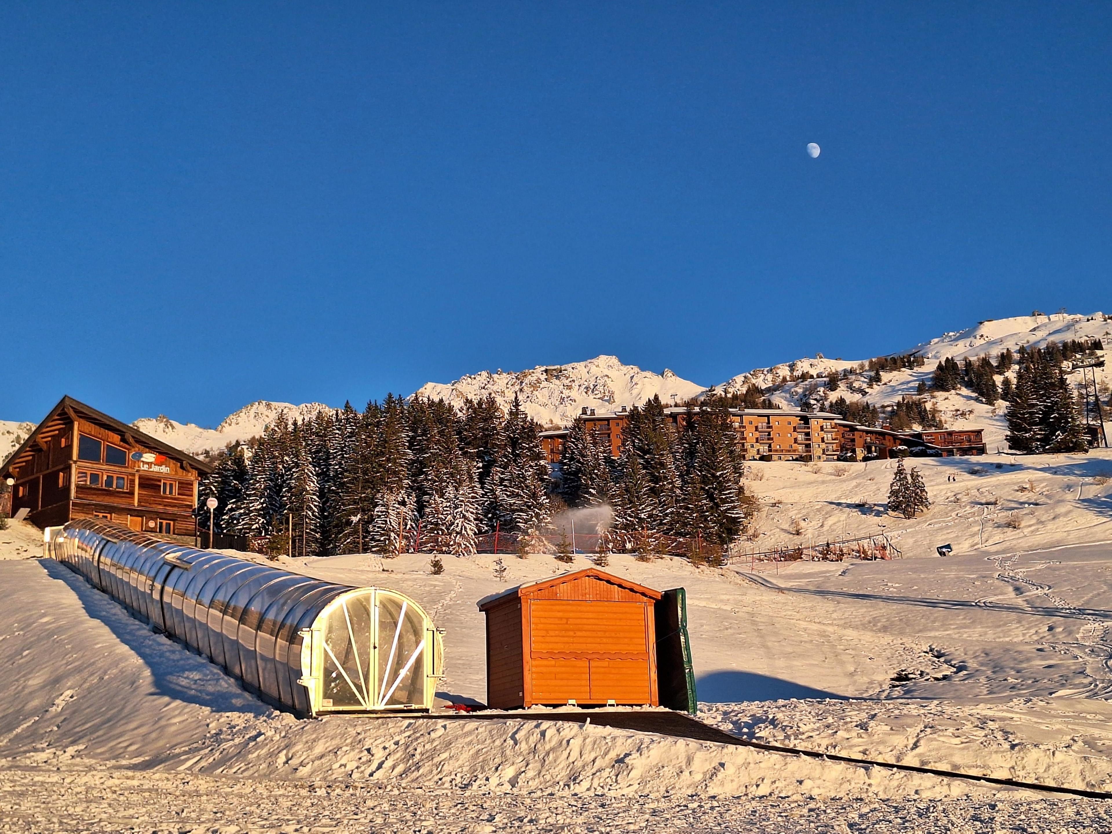 A wooden lodge with a clear view of snow-covered mountains and a moon in the sky.