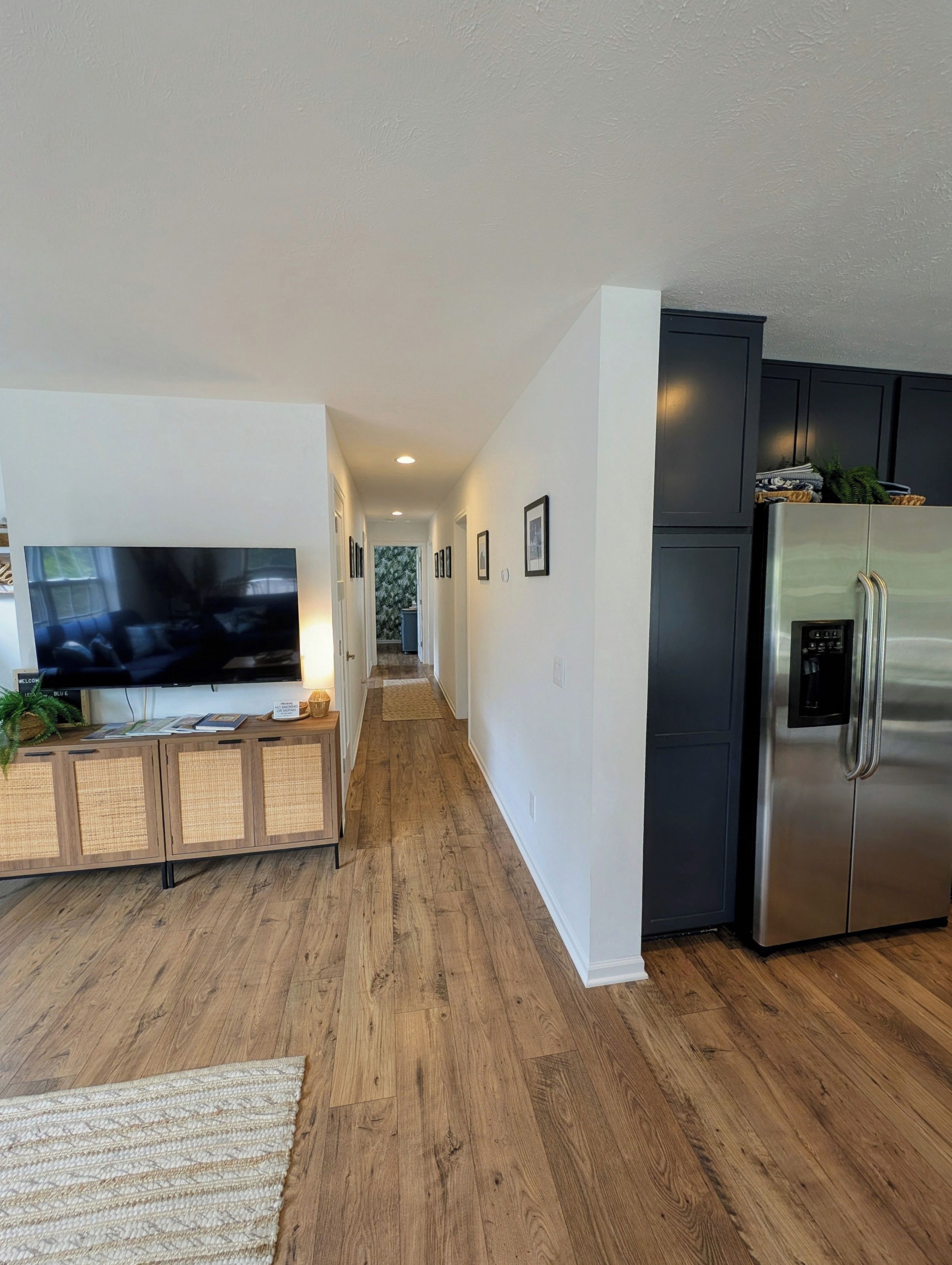 A modern kitchen with a stainless steel refrigerator, a wooden cabinet with a flat-screen TV, and a wooden floor.