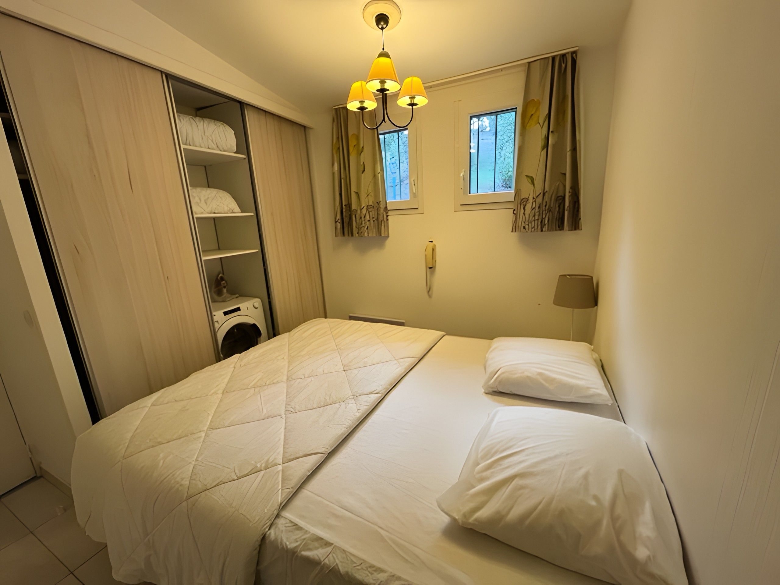 A hotel room with a bed, a wardrobe, a washing machine, and a window with curtains.
